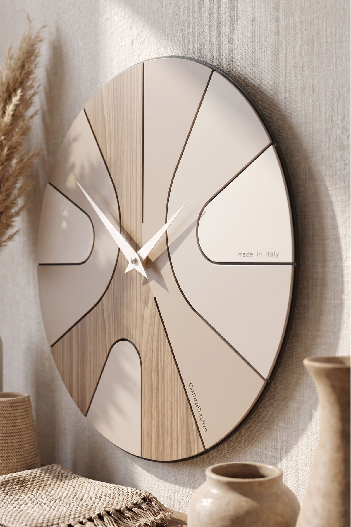 Close-up of the CalleaDesign Asym wall clock in Black Walnut and greige finish on a textured wall