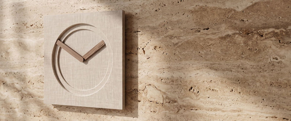 KAM Limited Edition wall clock with a linen-textured face and wooden hands on a warm travertine wall