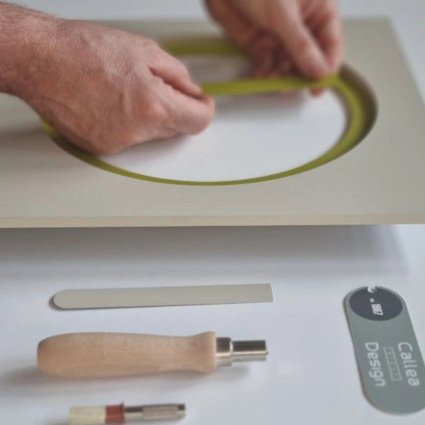 Hands fitting the green circular element of the KAM Linfa wall clock during assembly
