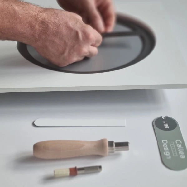 Hands assembling the circular grey detail of the KAM Nebbia wall clock in the atelier